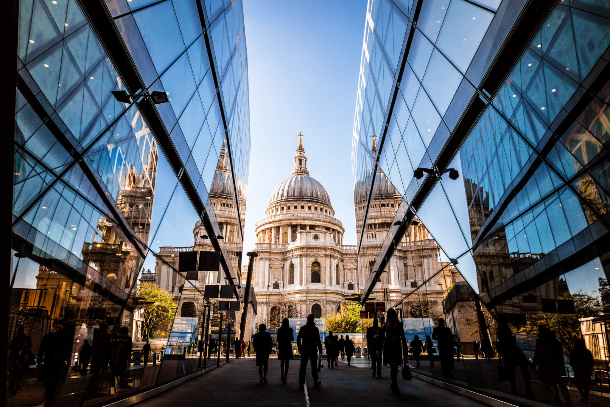 Color image depicting a crowd of people, thrown into silhouette and therefore unrecognisable, walking alongside modern futuristic architecture of glass and steel. In the distance we can see the ancient and iconic dome of St Paul's cathedral. Room for copy space.